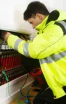 Technician in a neon yellow jacket inspecting wiring inside an open electrical panel
