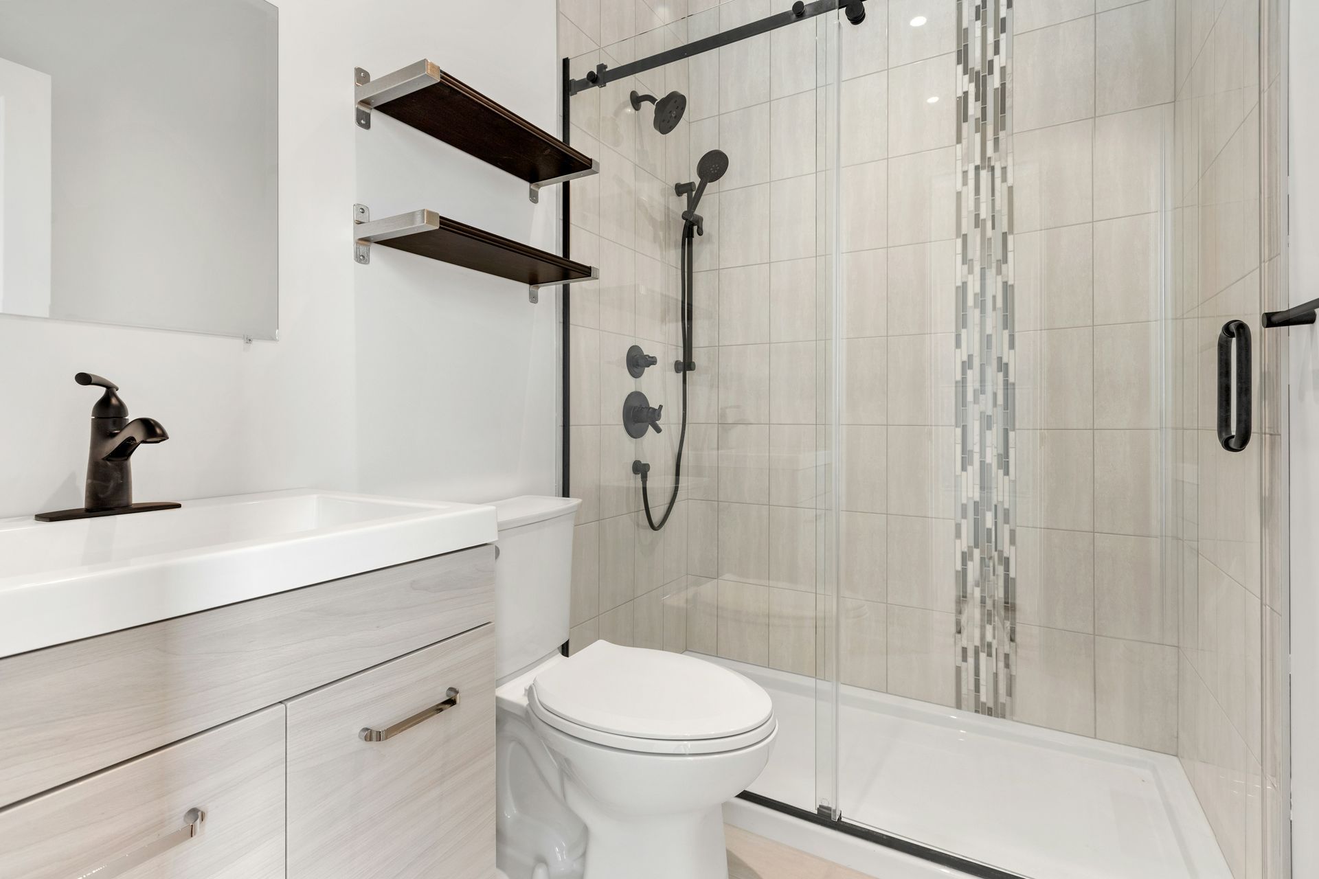 Modern white bathroom with vanity, toilet, glass shower, and dark wood shelves