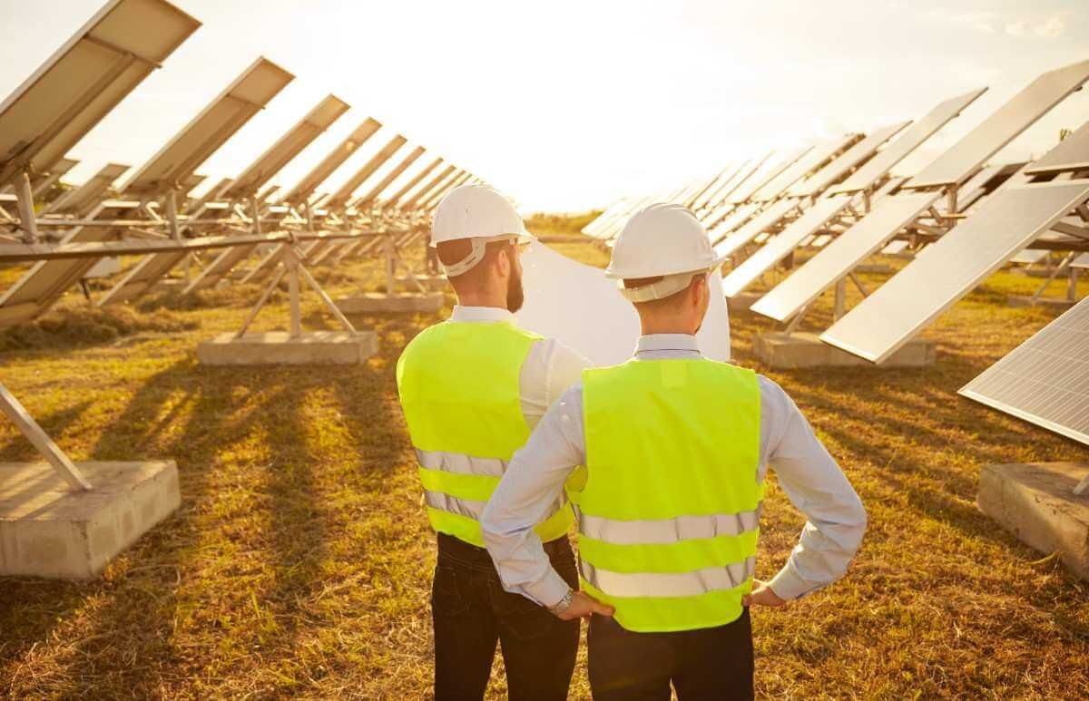 Two workers in neon vests inspecting rows of solar panels at sunset