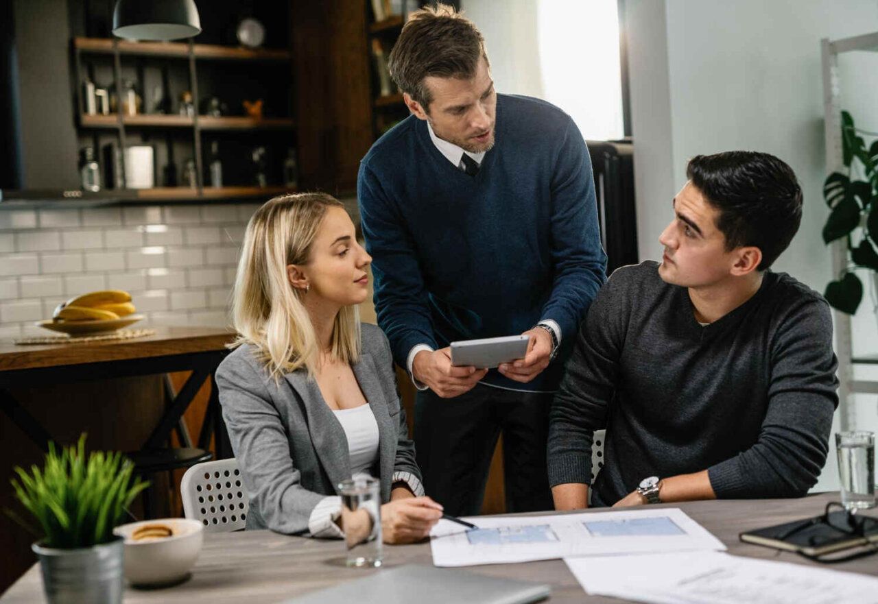 Three coworkers discussing documents at a desk in a modern office kitchenette
