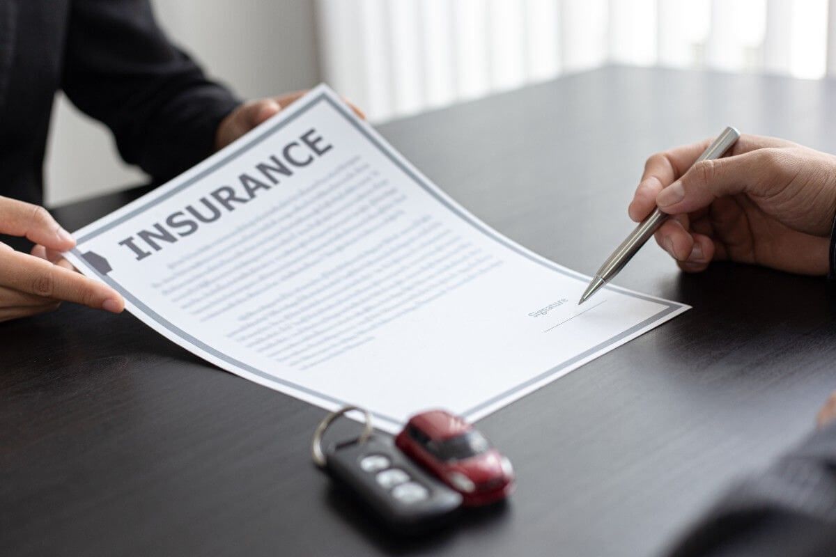 Insurance form being signed at a desk beside car keys