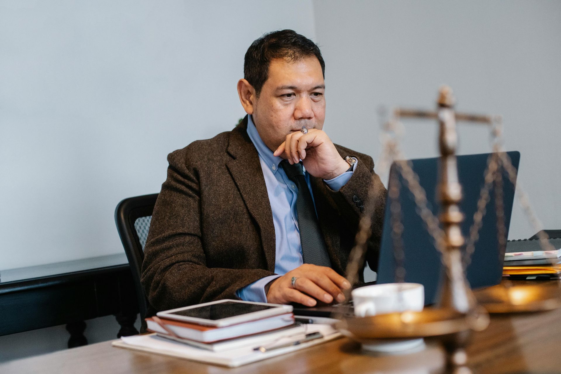 Man seated at a desk, working on a laptop in a conference room, with books and a gavel nearby.
