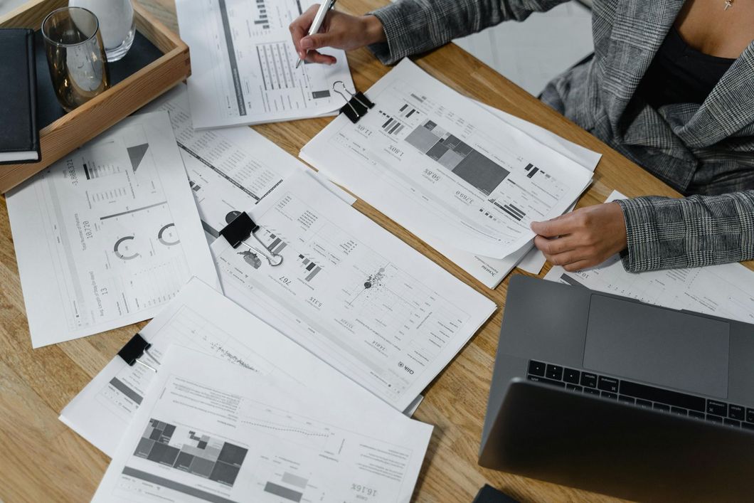 Hands reviewing printed charts and reports on a desk beside an open laptop