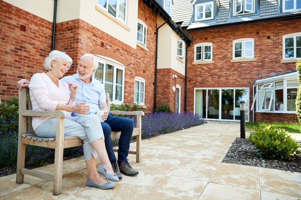 An Elderly Couple is Sitting on a Bench in Front of a Brick Building — ASpect Wall & Floor Tiling in Tuncurry, NSW