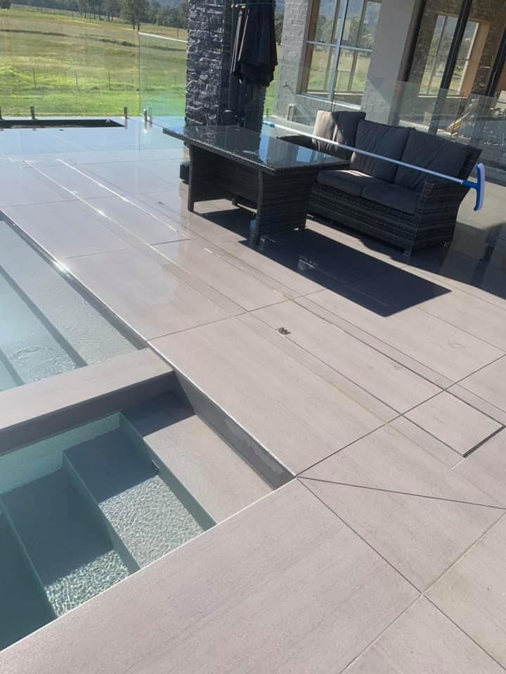 A Patio With a Couch , Table and Chairs Next to a Pool — ASpect Wall & Floor Tiling in Tuncurry, NSW