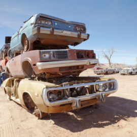Three stacked, salvaged vintage cars in a desert junkyard under a clear blue sky.