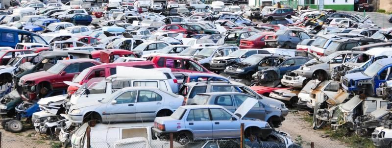 A sprawling, cluttered junkyard filled with rows of stacked, damaged cars in various colors and models.