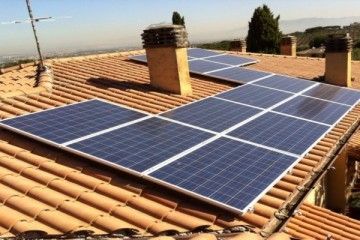 Pannelli solari installati su un tetto di tegole in terracotta con camini in mattoni sotto un cielo sereno