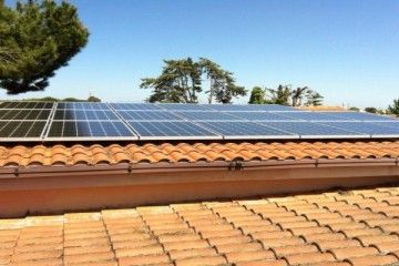 Pannelli solari su un tetto di tegole di terracotta sotto un cielo azzurro e limpido.