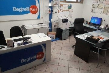 Banco reception in un ufficio beige con computer, sedie e insegna di Beghelli Point.