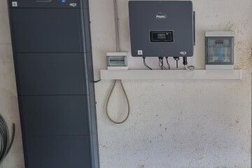 Inverter solare a parete e apparecchiature elettriche accanto a un alto armadio nero per batterie.