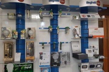 Stand fieristico con torri espositive verticali blu, campioni di prodotto e cartelli su una parete bianca.