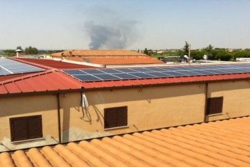Pannelli solari sui tetti di edifici color sabbia sotto un cielo limpido in una soleggiata zona urbana.