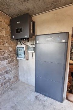 Apparecchiature elettriche a parete: inverter, quadro elettrico e grande armadio grigio per batterie in una stanza di cemento.
