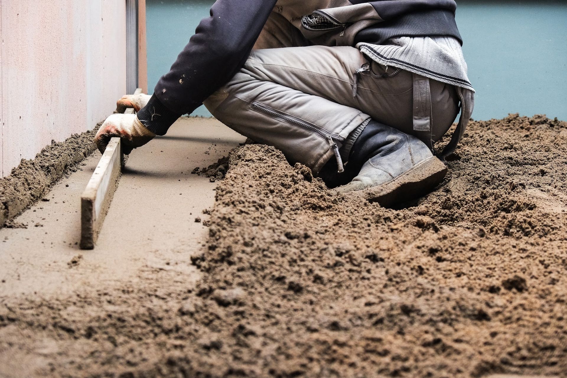 Worker smoothing wet concrete with a trowel along a wall outdoors