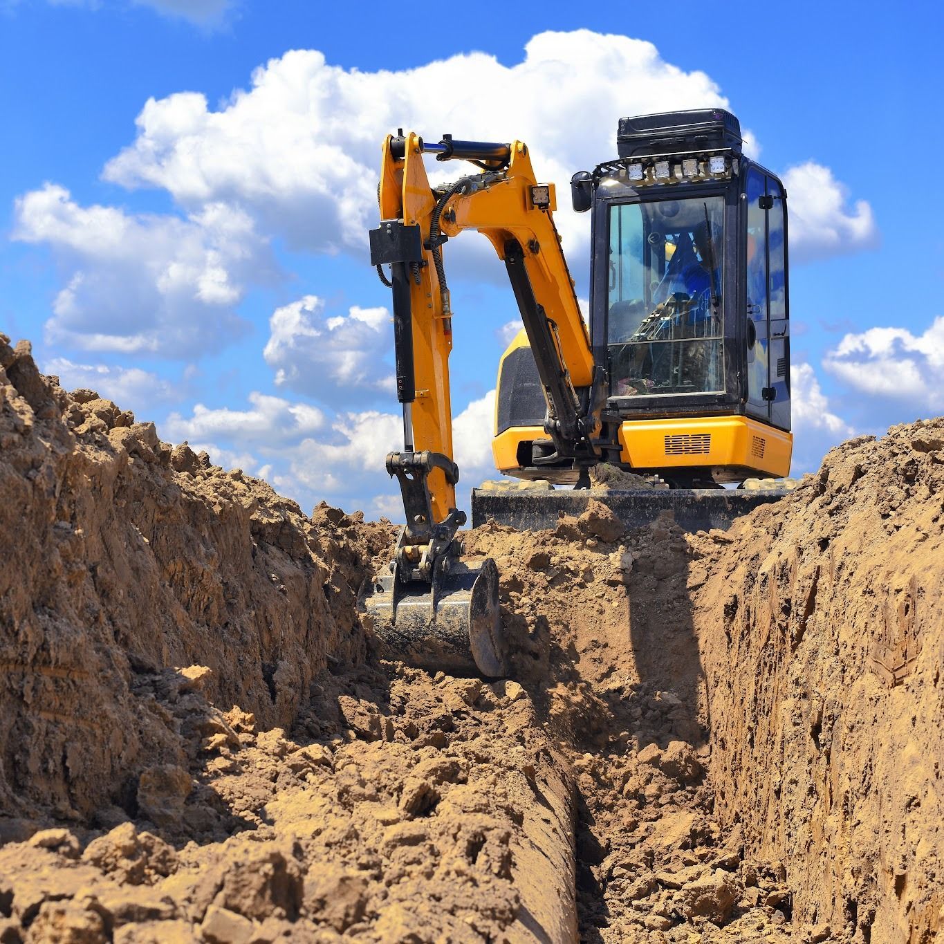 Yellow excavator digging a trench in a dirt construction site under a blue sky