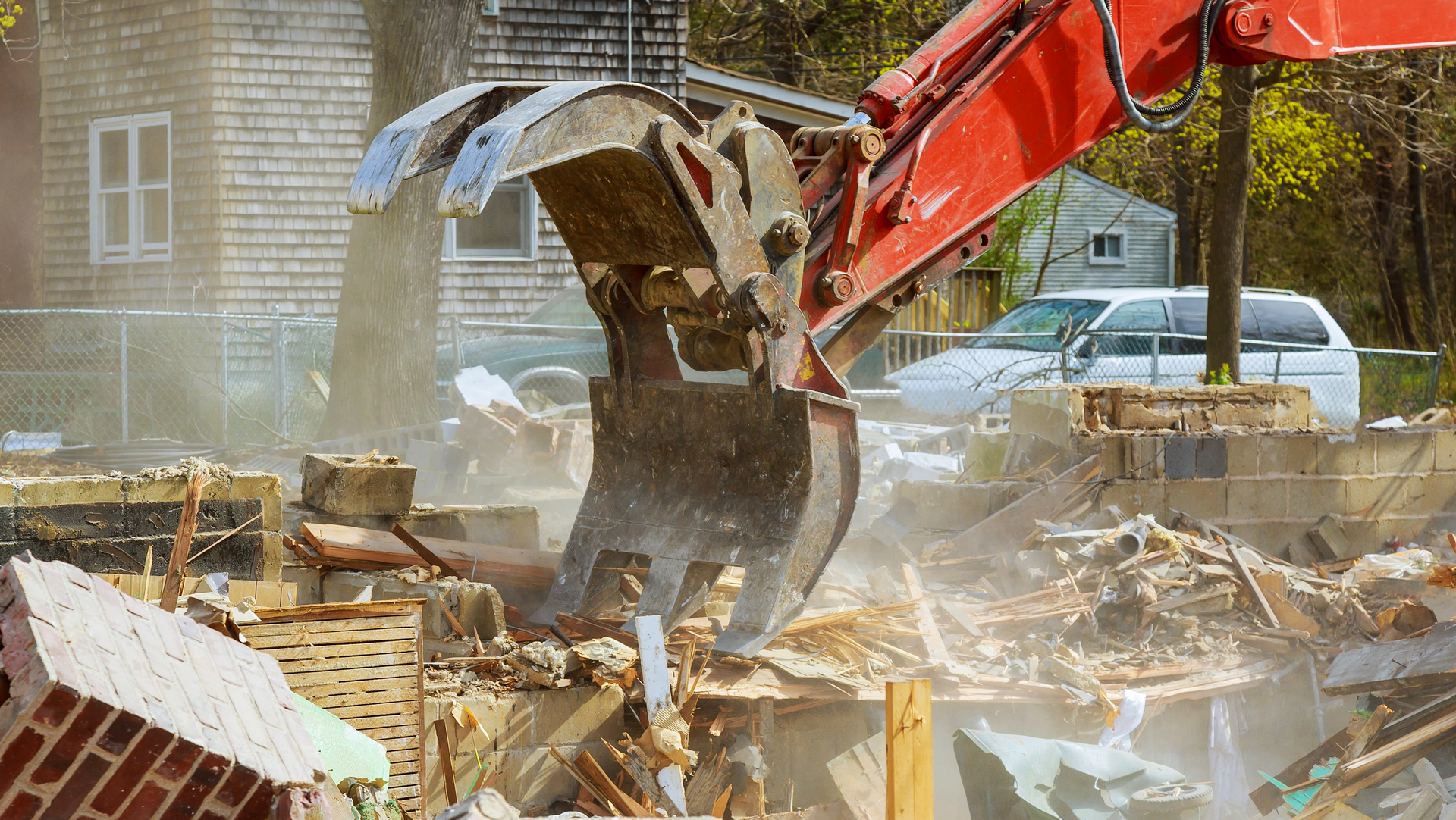 Red excavator demolishing a pile of rubble at a construction site, dust flying in the air.