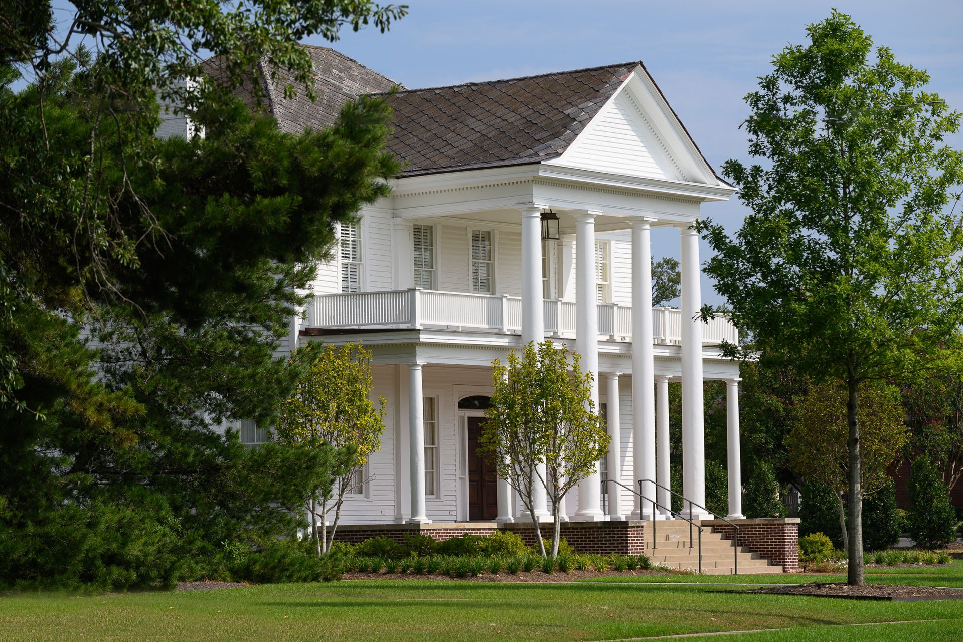 A large white house with columns is surrounded by trees