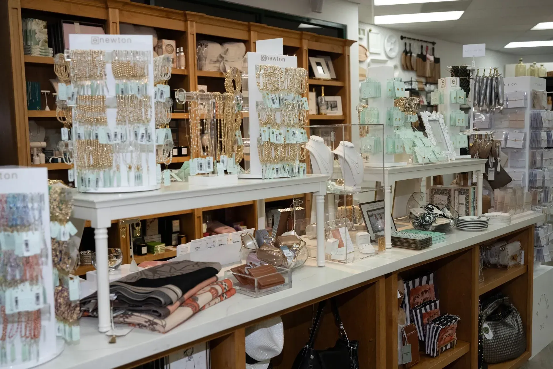 Boutique display of jewelry, candles, and folded textiles on white shelves in a shop
