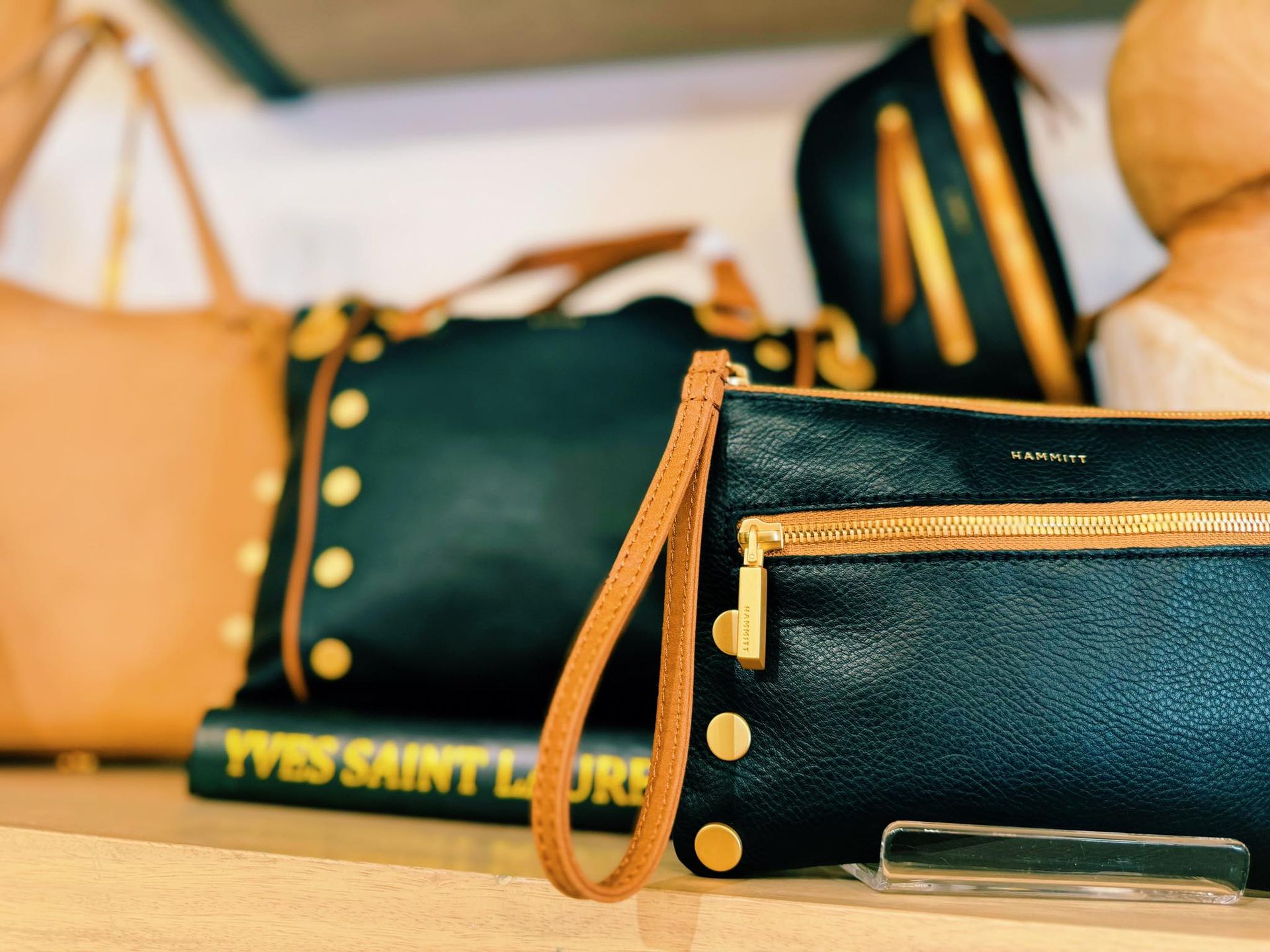 Close-up of leather handbags in various colors, with gold hardware and details, displayed on a shelf.