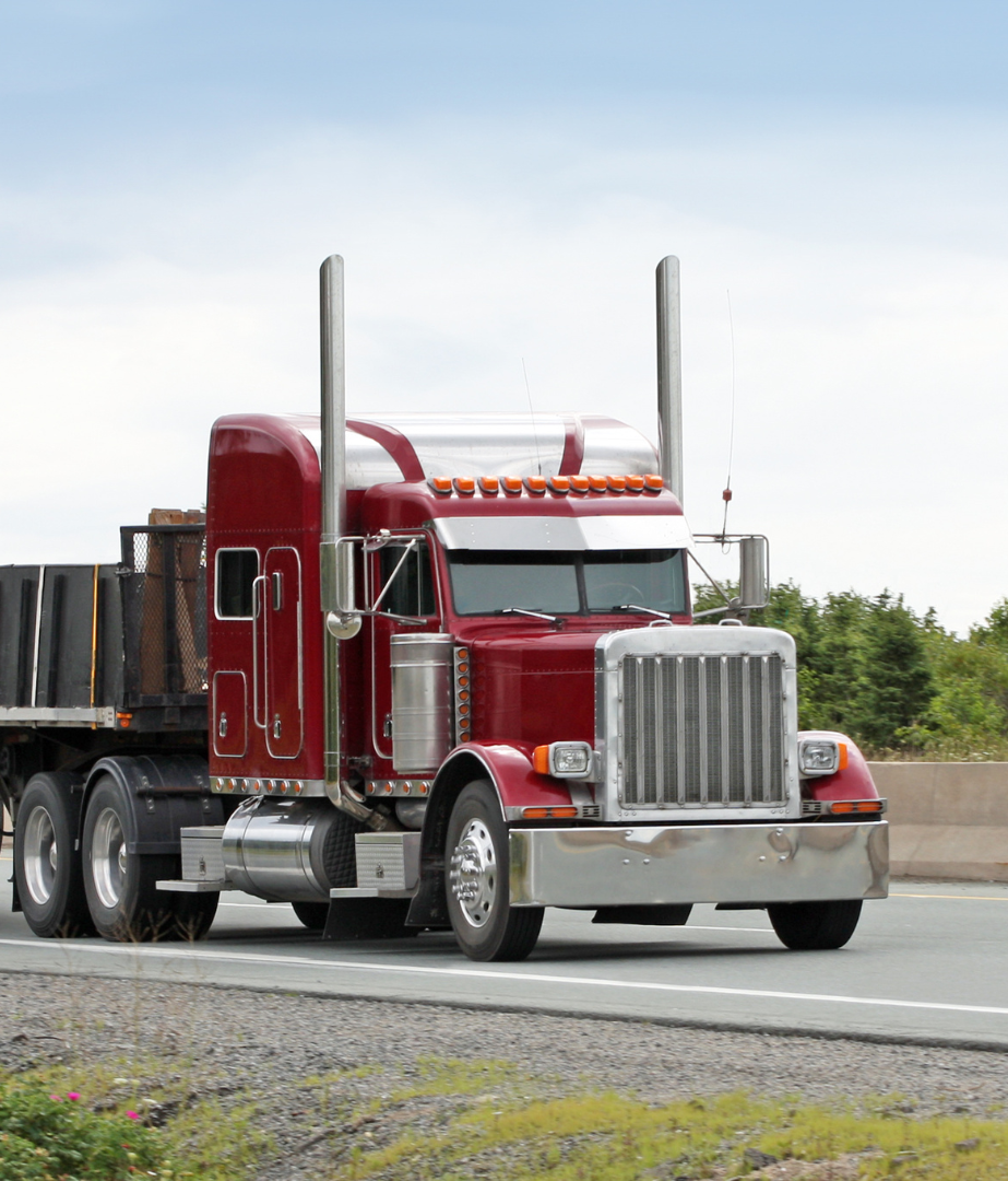 A red semi truck is driving down a highway.