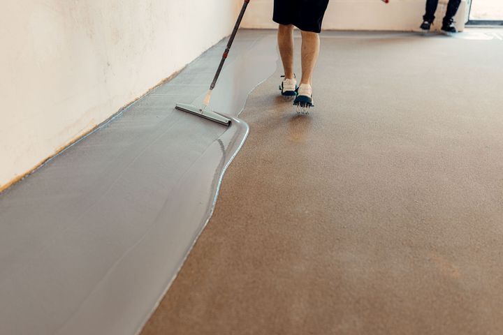 Person painting a gray floor edge beside a tan walkway in a hallway