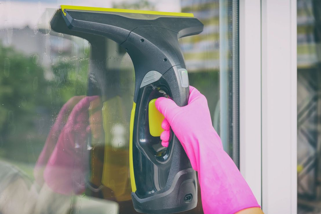 Una mano guantata usa un tergivetro giallo e nero per pulire una finestra di vetro.