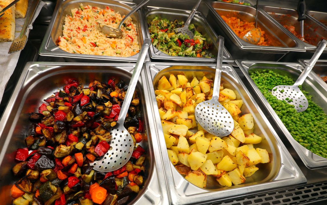 Un buffet con vassoi di piatti caldi assortiti, tra cui patate arrosto, verdure e carne in salsa.