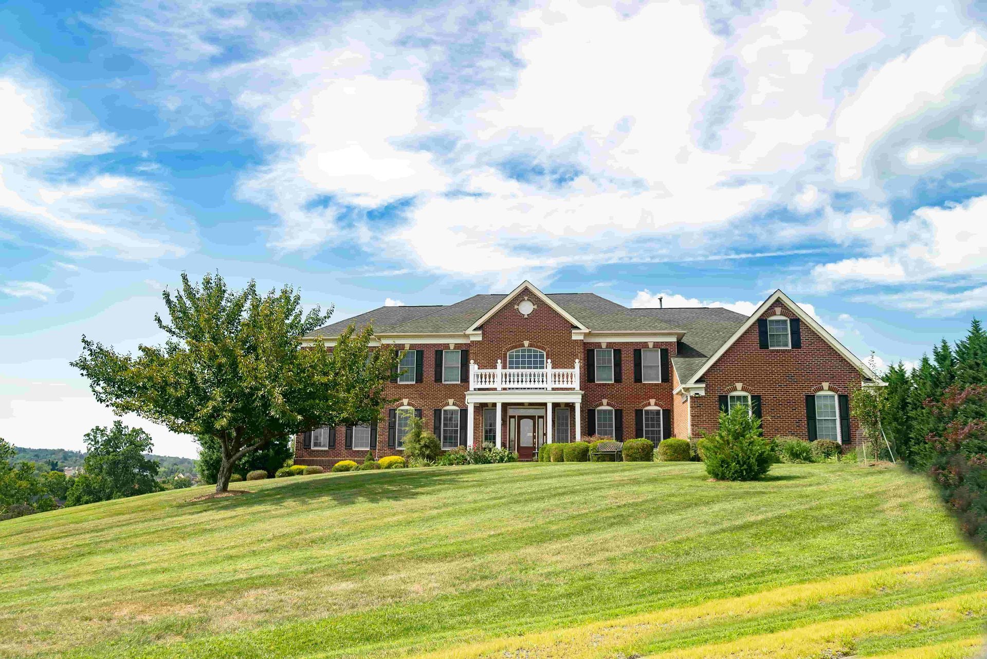Large brick house on a green lawn under a partly cloudy sky