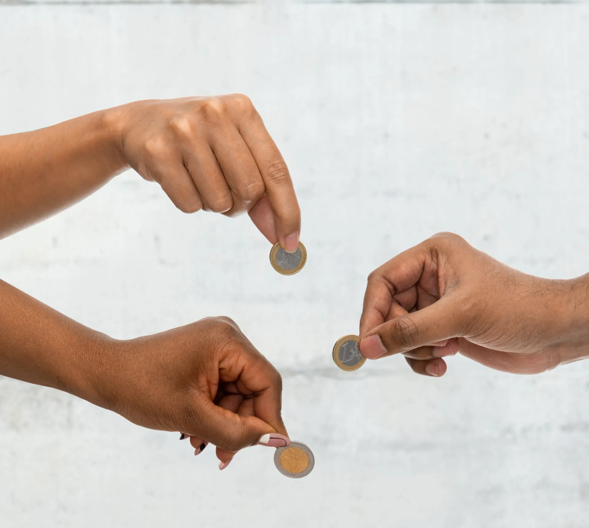 Três mãos trocando pequenas moedas contra um fundo claro e liso.