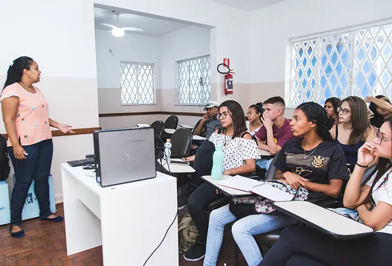 Professor apresentando conteúdo para alunos em sala de aula com projetor e cadernos.