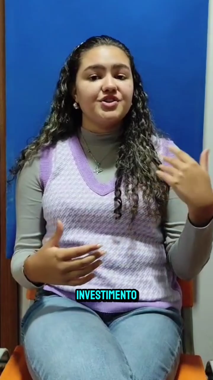 Mulher sentada contra um fundo azul, falando com uma das mãos levantadas