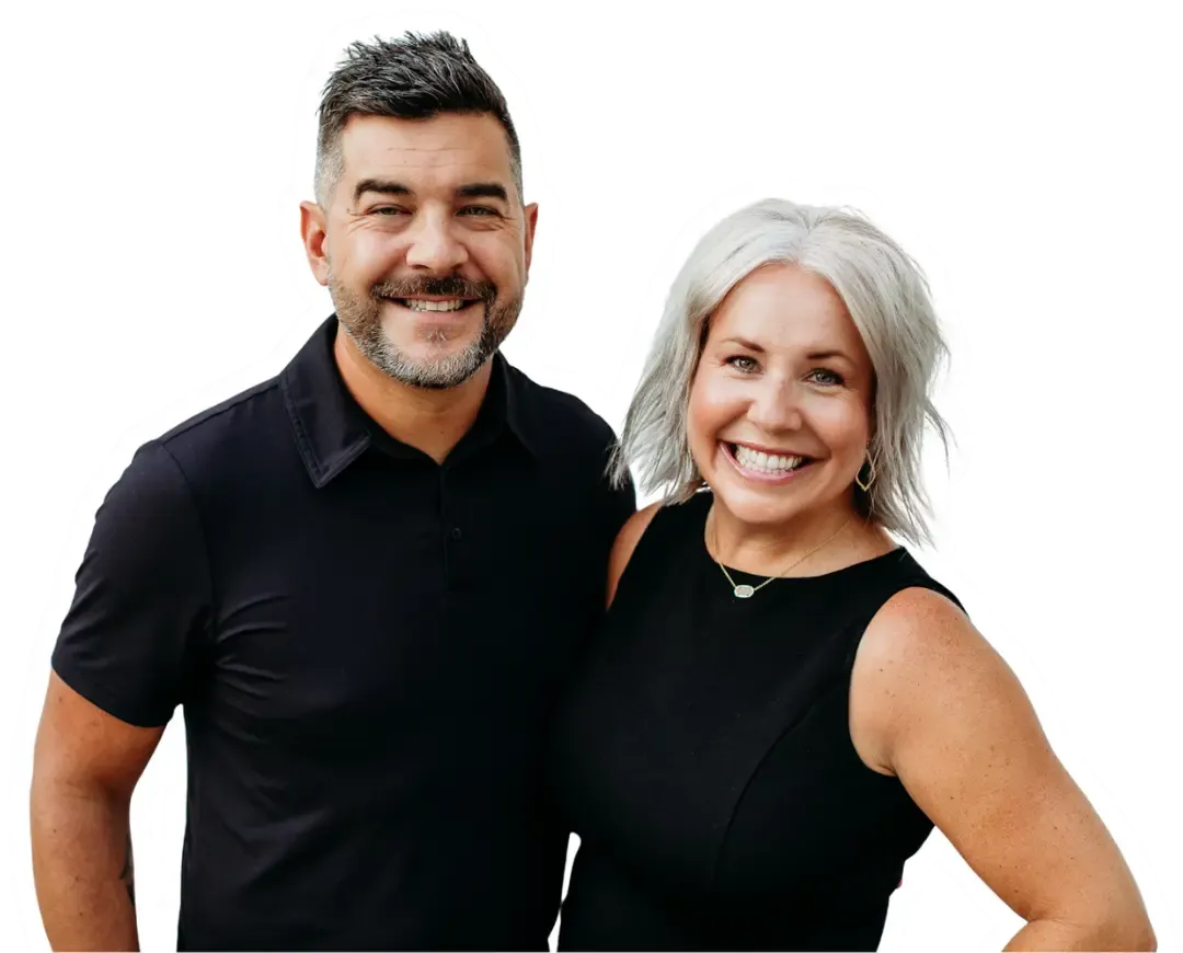 Smiling couple posing together, man with dark hair, woman with silver hair, both in black.