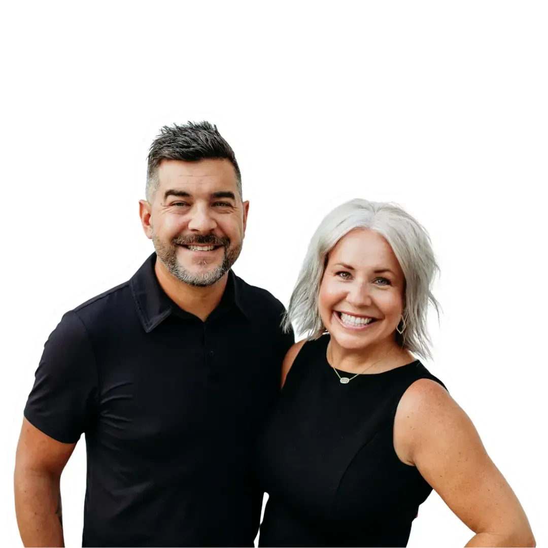 Smiling couple posing together, man with dark hair, woman with silver hair, both in black.