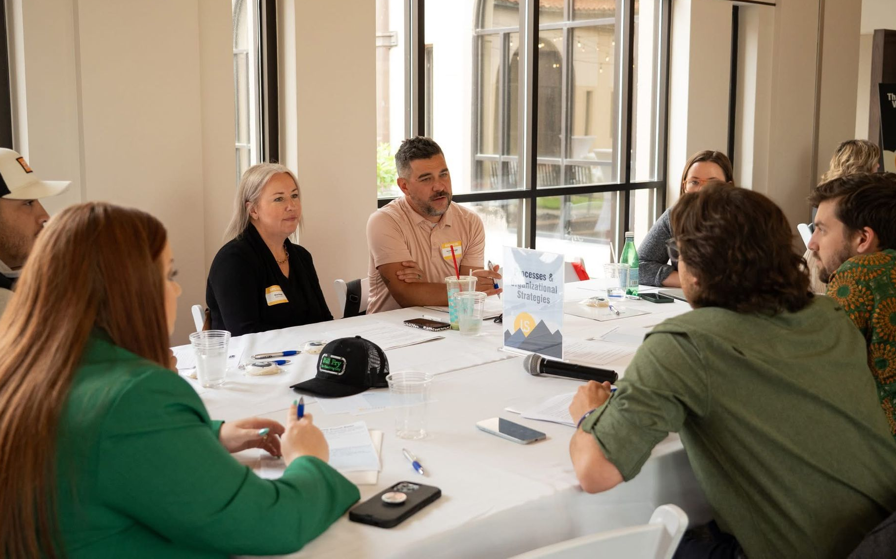 Small group meeting around a white table in a bright room, discussing with papers and a camera on the table