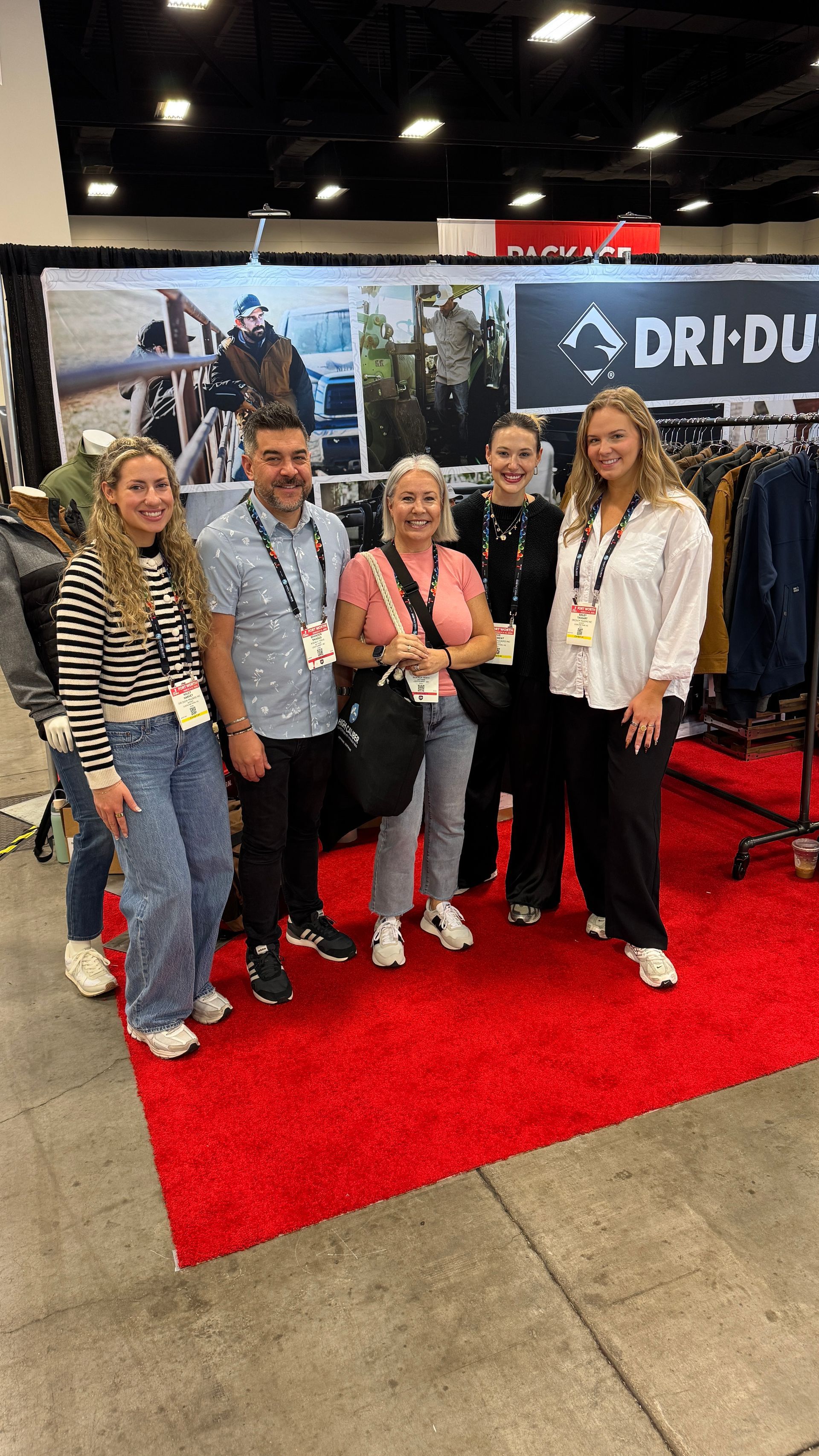 Five people pose on a red carpet at a trade show booth with a car backdrop.