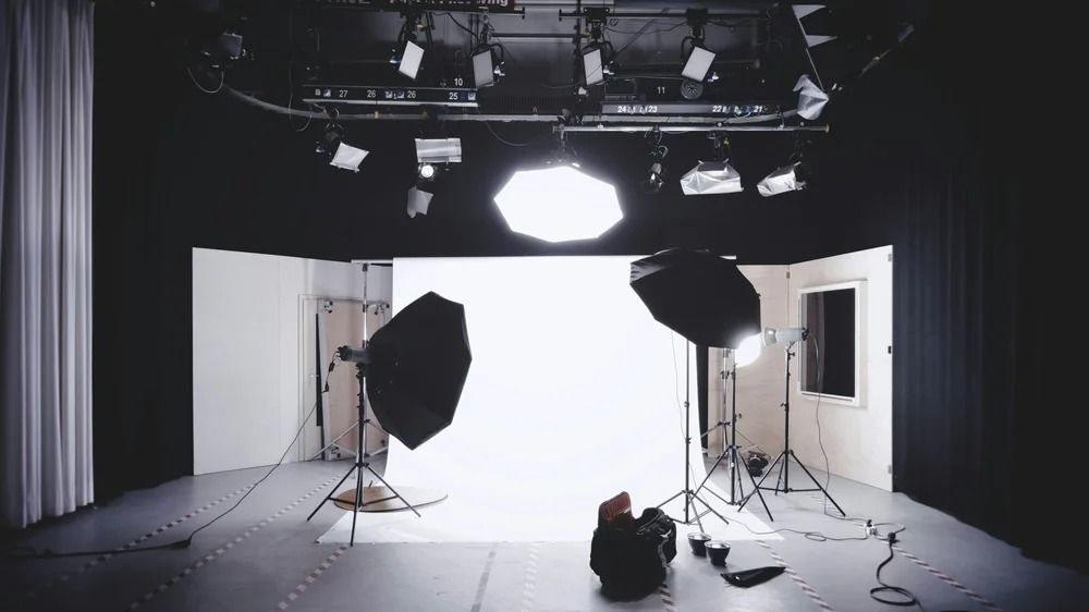 Photo studio with white backdrop, lighting equipment, and a person sitting on the floor.