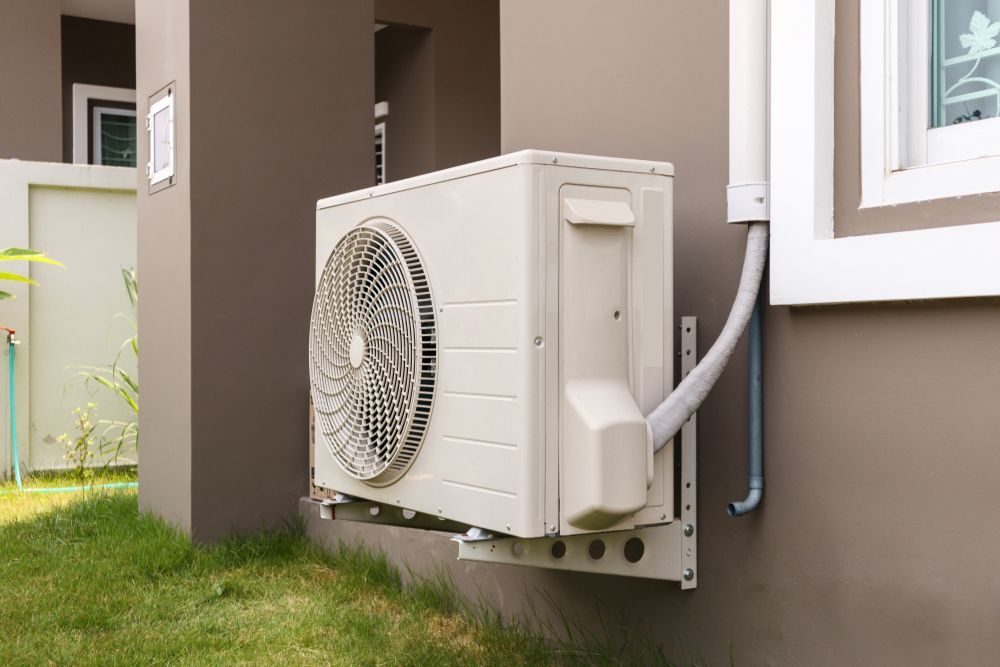 White Air Conditioner Unit Mounted on a Brown Exterior Wall — RedJak Air Conditioning Services in Underwood, QLD