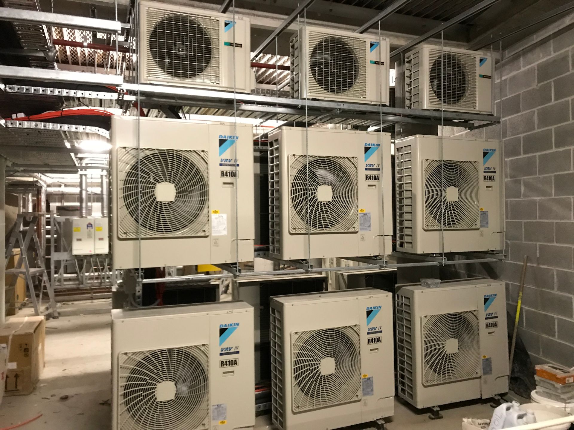 Air conditioning units mounted on racks in a room with cinder block walls.