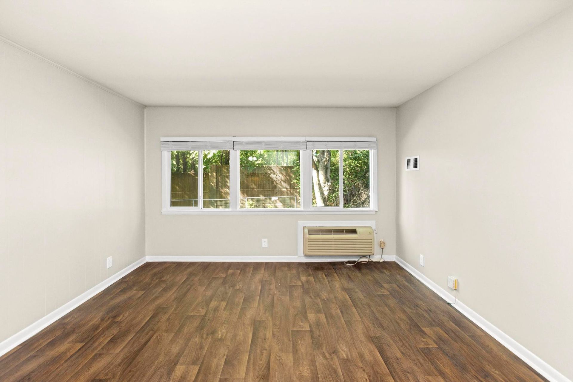 Empty room with wood flooring, large window, and wall-mounted air conditioner