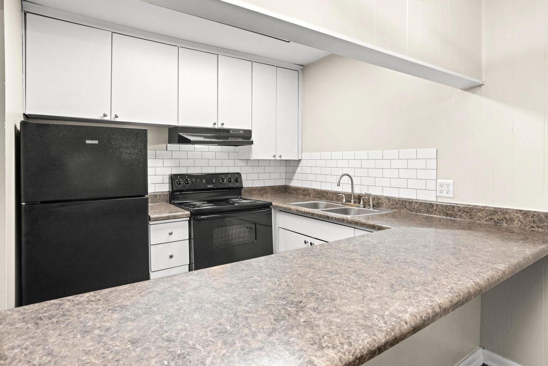 Empty modern kitchen with black appliances, white cabinets, and speckled granite countertops