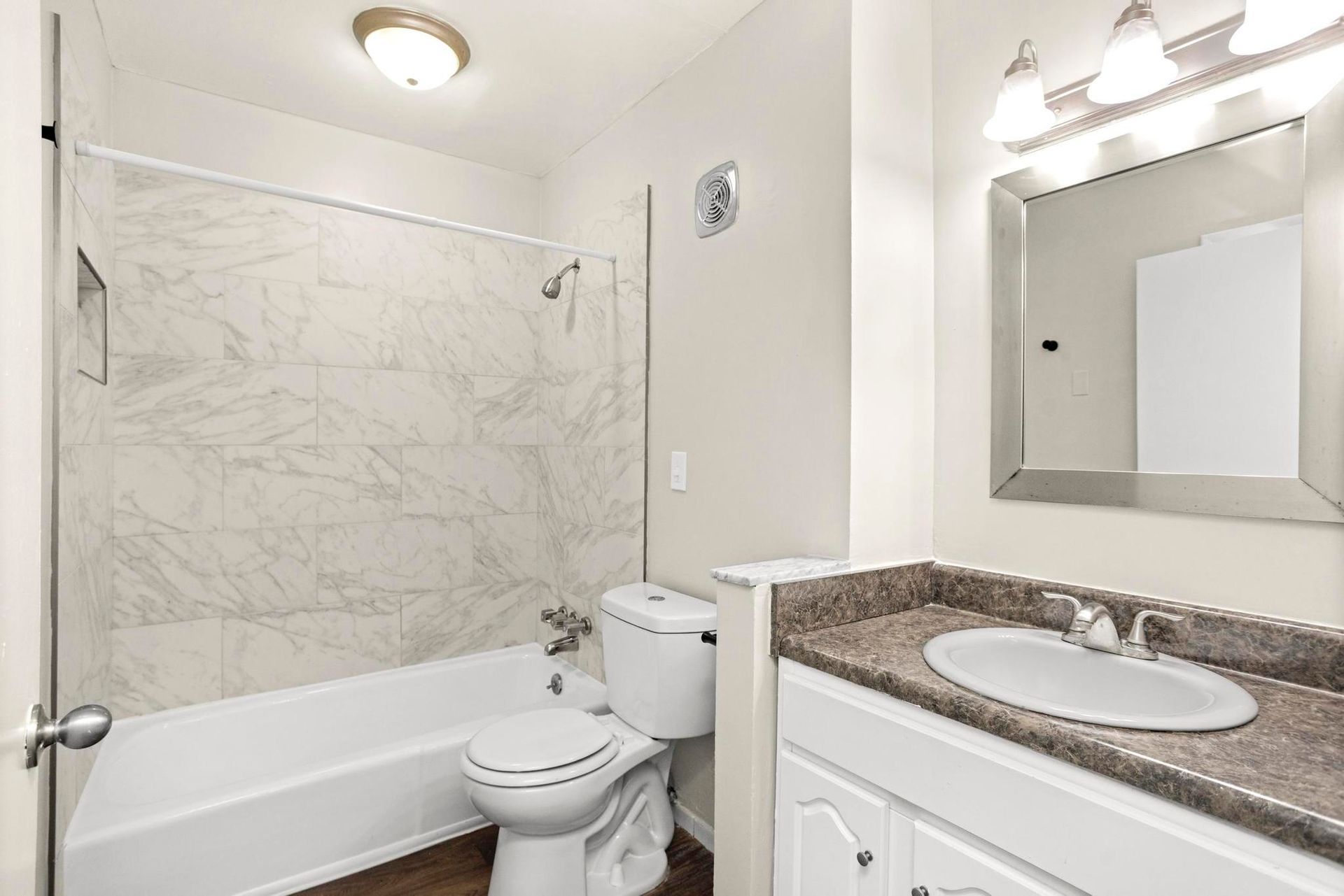 Bright bathroom with a bathtub, toilet, and granite vanity with a mirror.