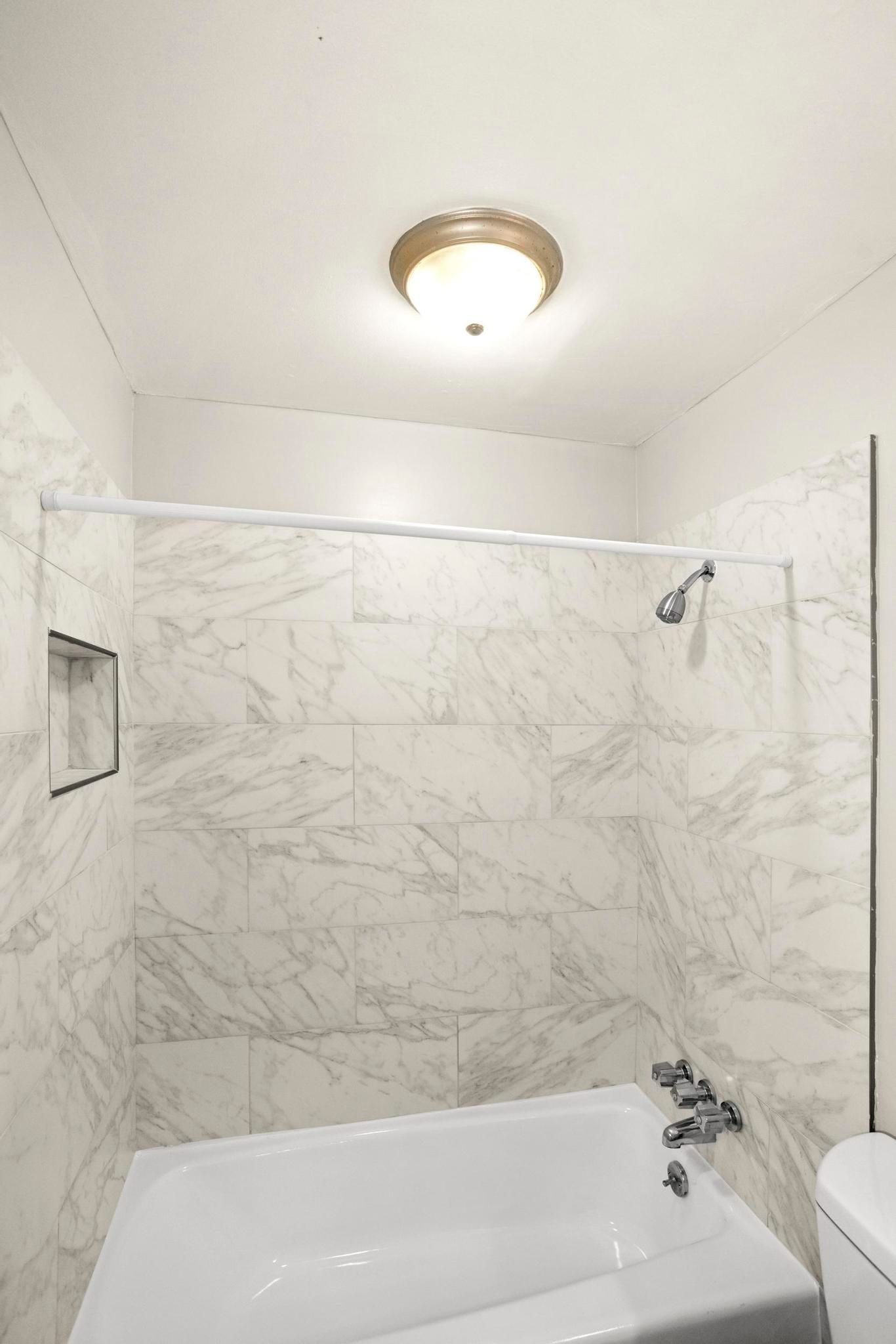 Small bathroom with marble-pattern shower walls, bathtub, toilet, and ceiling light.