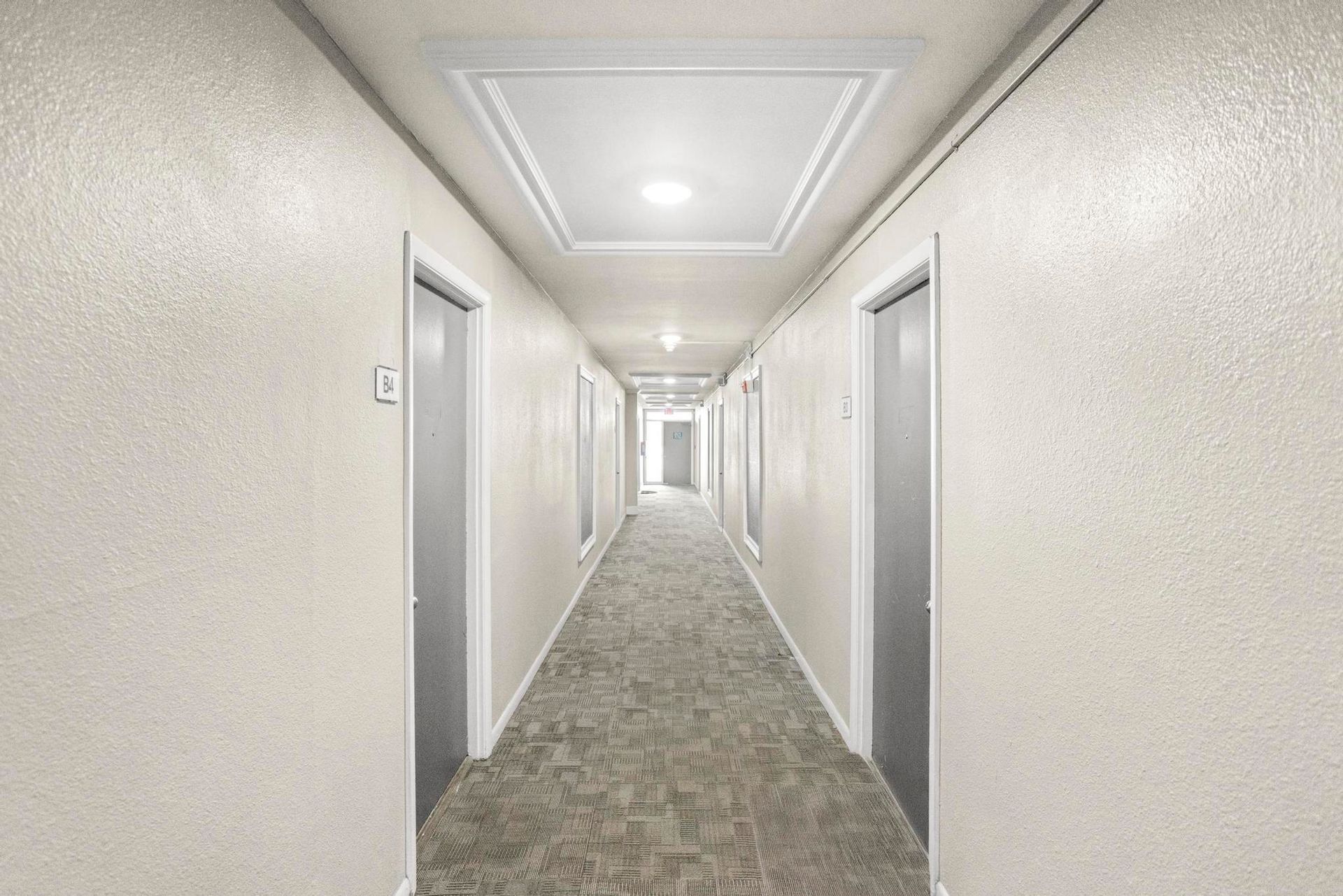 Long beige hotel hallway with gray carpet and white doors on both sides