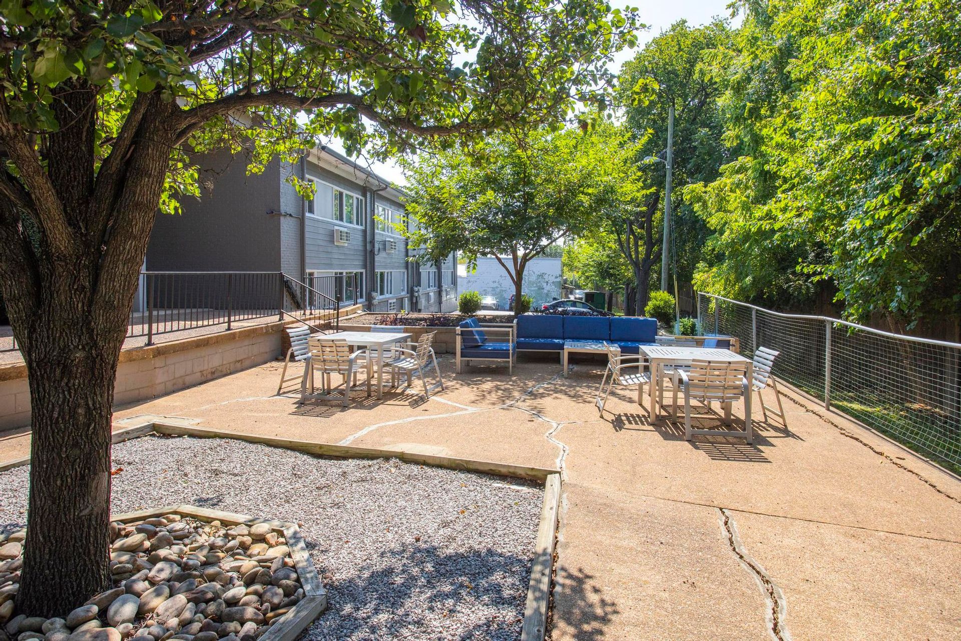 Outdoor patio with picnic tables, string lights, and trees beside a building on a sunny day