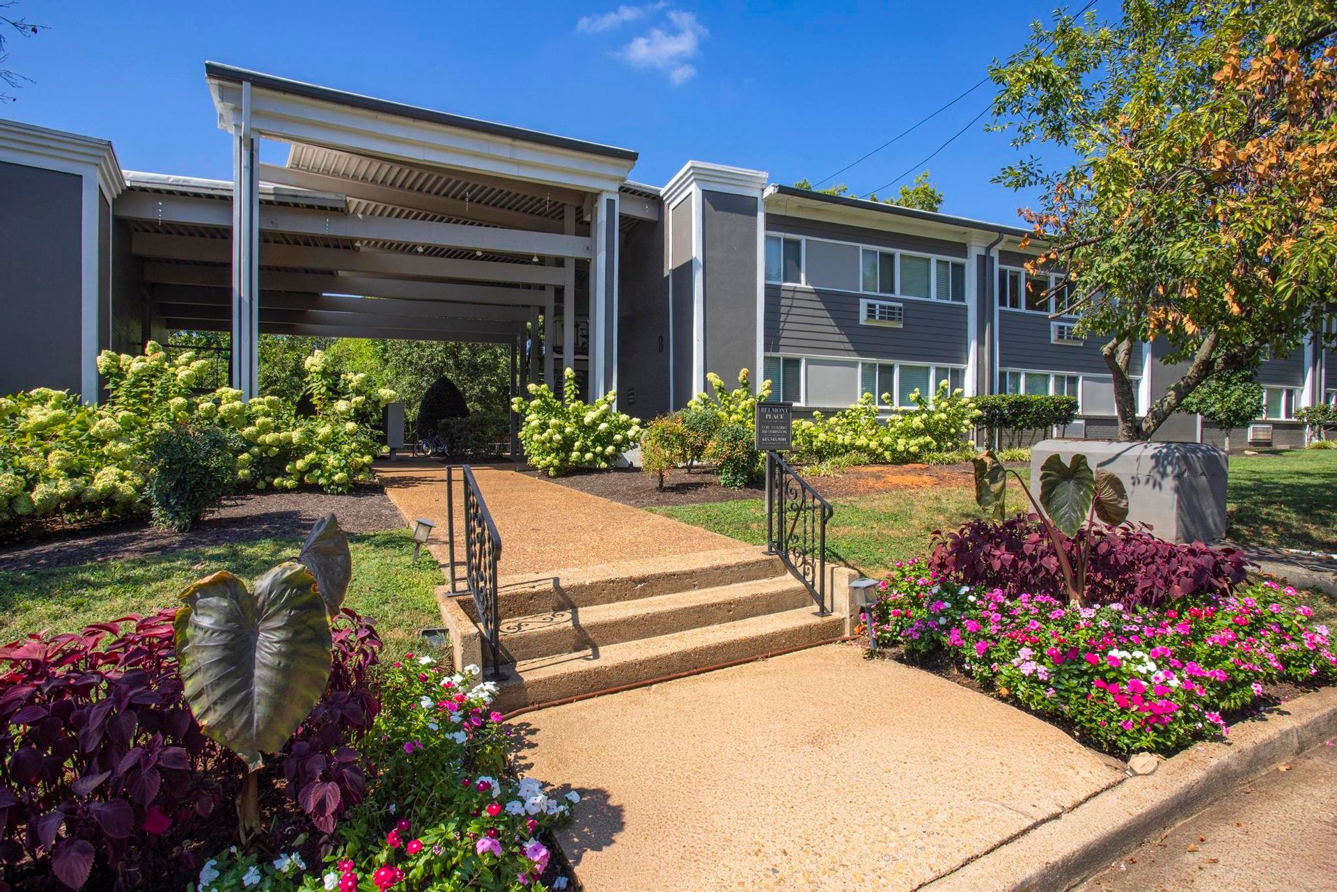 Landscaped apartment entrance with steps, flower beds, and a covered walkway