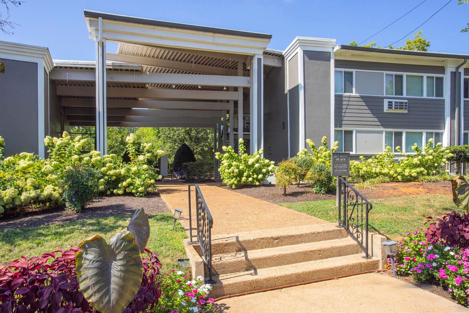 Apartment complex entrance with stairs, ramp, and landscaped garden under a covered walkway