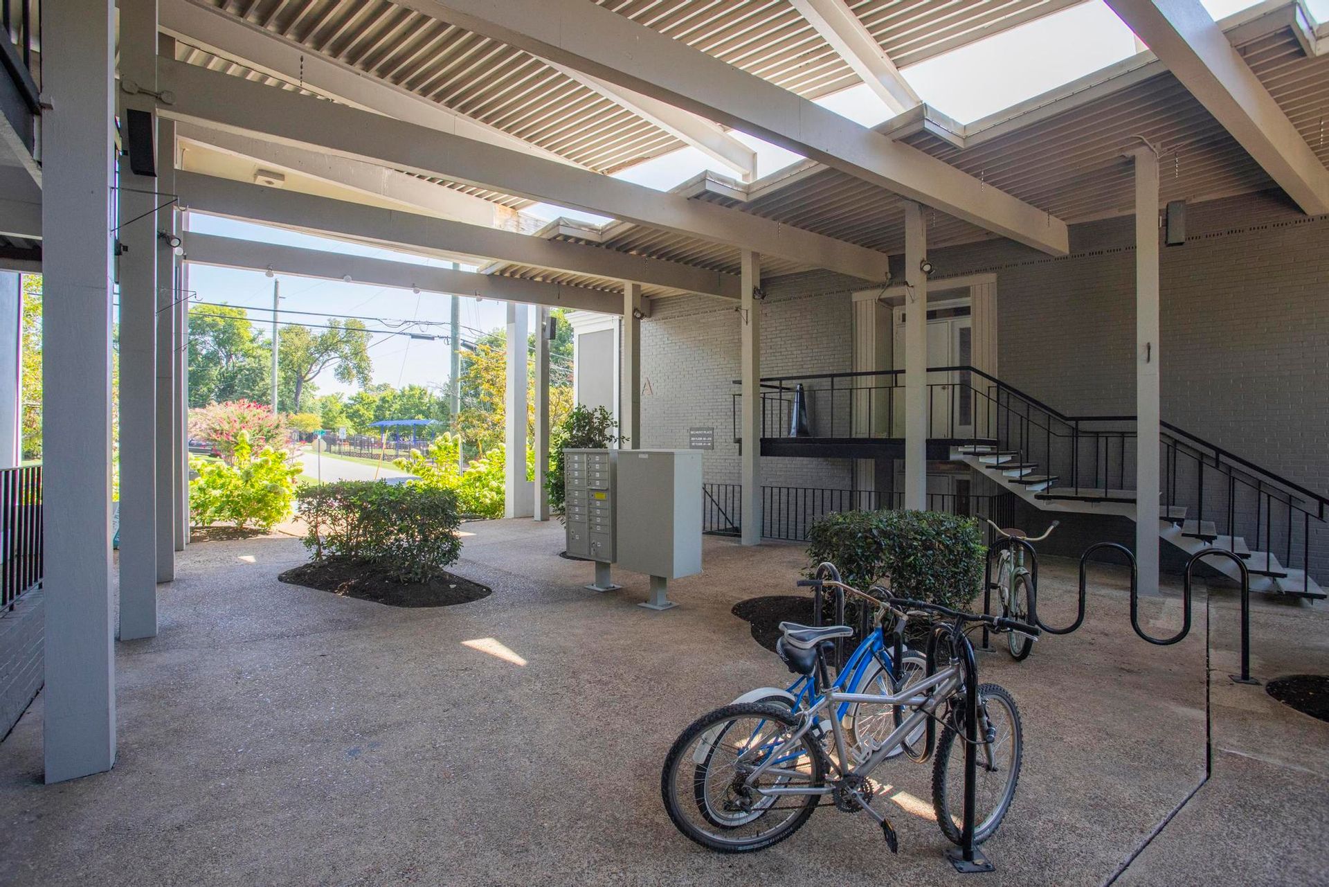 Covered walkway with parked bicycles, stairs, and sunlit courtyard plants