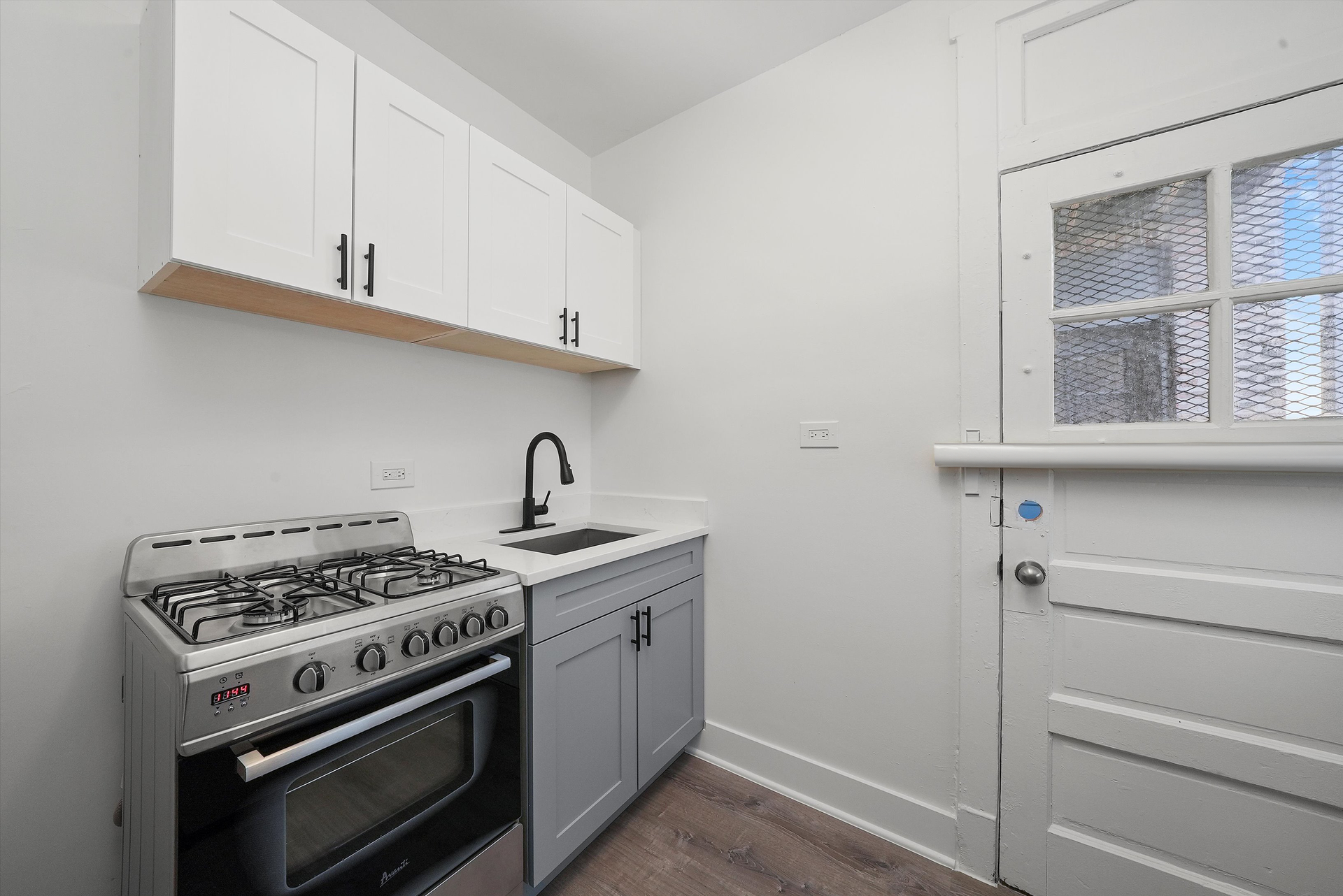 Small, updated kitchen with stove, sink, cabinets, and a door with a window. Bright and airy space.