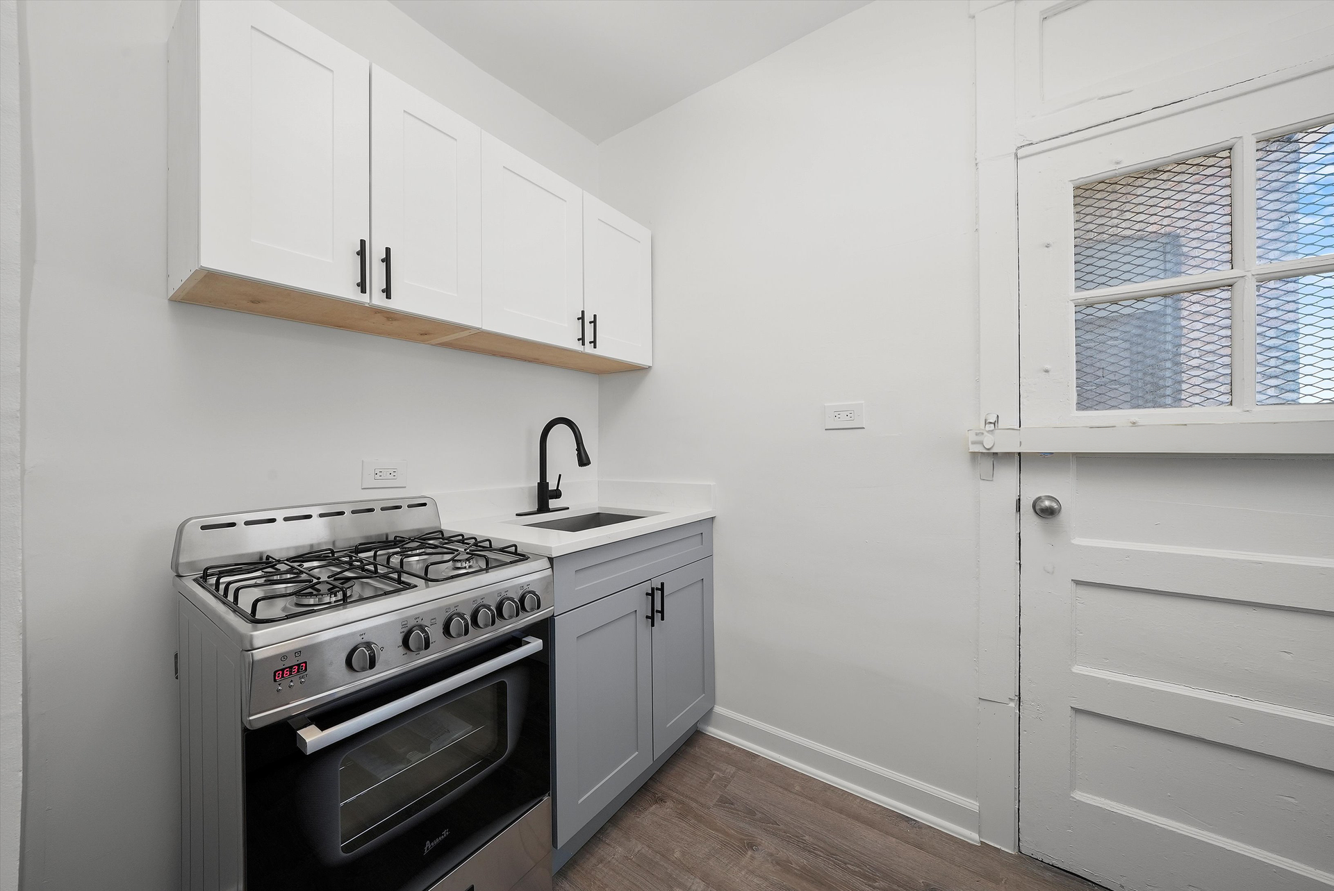 Small, updated kitchen with white cabinets, a gray sink base, a stove, and a windowed door.